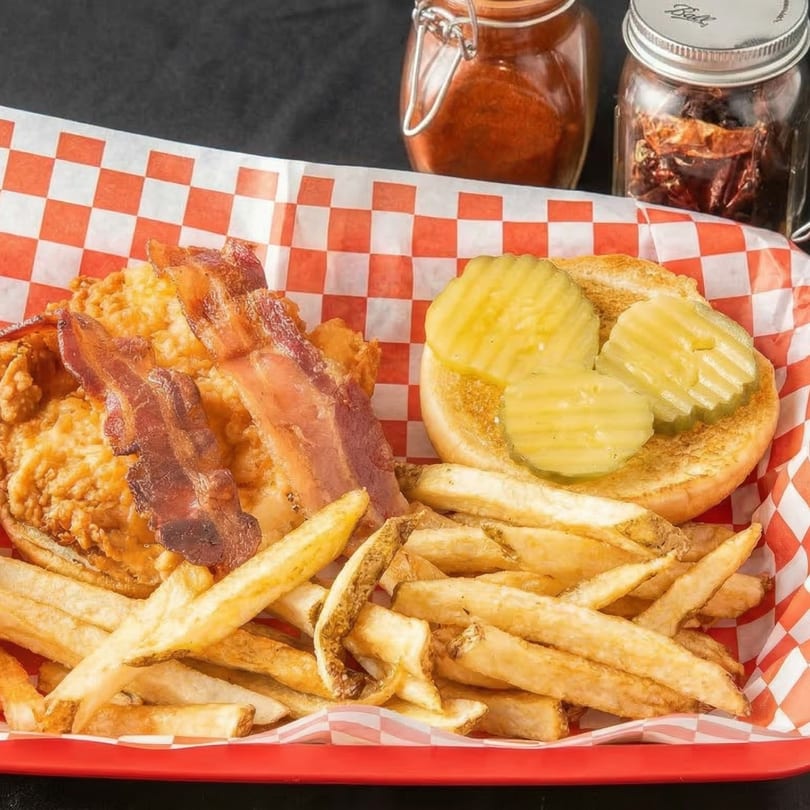 Crispy fried chicken sandwich with bacon, pickles, and a side of golden french fries.