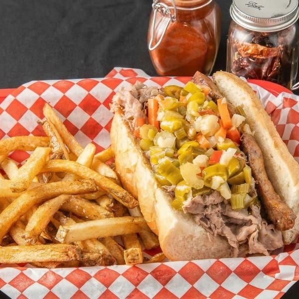 Chicago-style Italian beef sandwich with giardiniera and a side of golden fries in a red checkered basket.